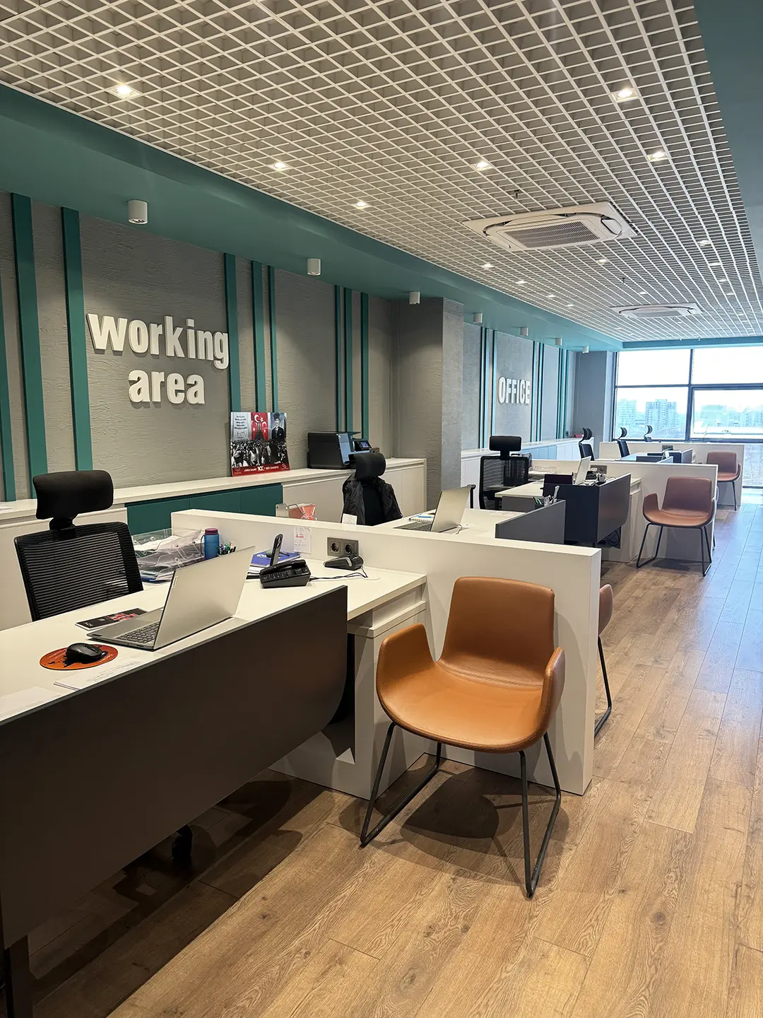 İlkiş Elektrik açık ofis alanı, Working Area tipografi, turkuaz dikey şeritler, beyaz masalar ve grid tavan