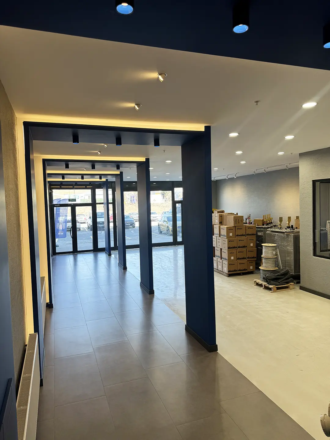 İlkiş Elektrik ofis giriş holü, koyu mavi çelik kolonlar, gizli LED şerit aydınlatma ve cam cephe showroom girişi
