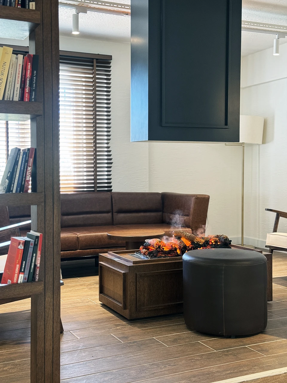 Kafe lounge alanı — deri koltuk, koyu ahşap ve elektrikli şömine tasarımı