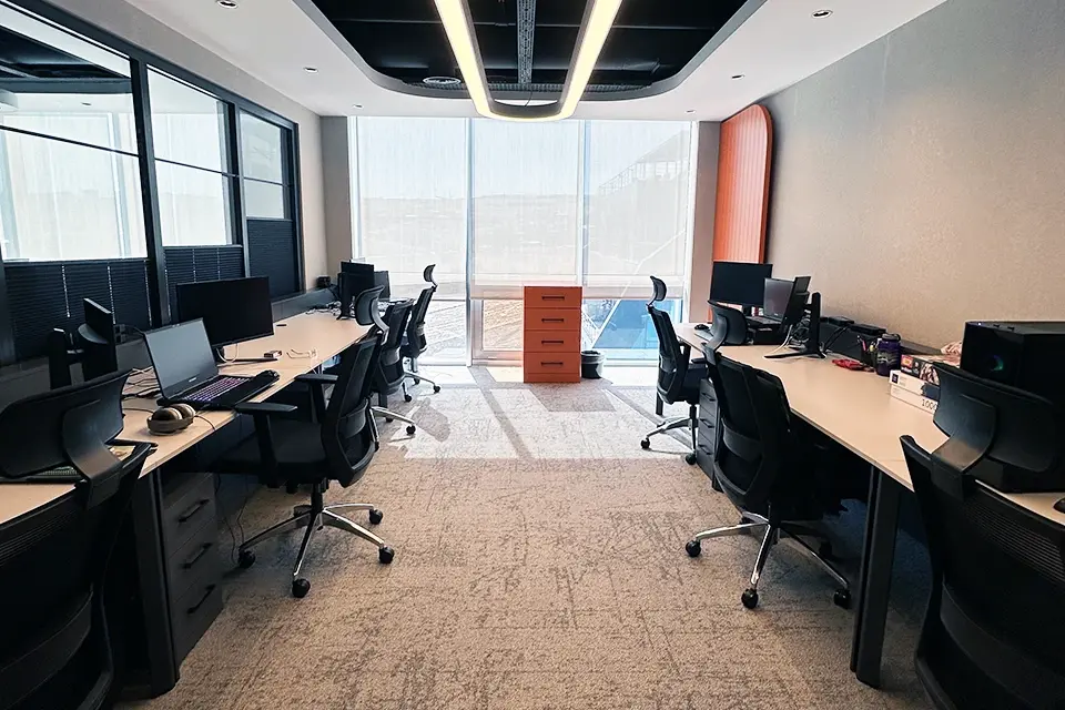 Loop Games Ofis açık ofis çalışma alanı, simetrik masa düzeni, organik formlu LED avize ve turuncu vurgu dolabı