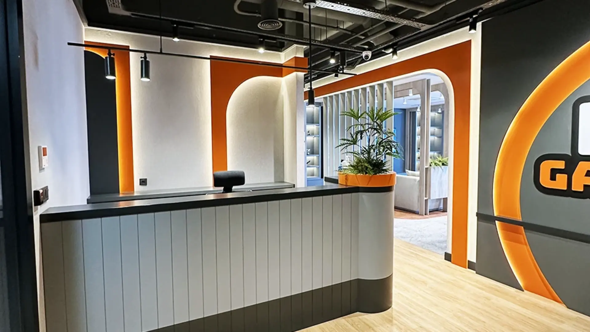 Loop Games Ofis resepsiyon alanı, dikey lamelli resepsiyon bankosu, turuncu kemerli geçişler ve LED ışıklı Loop Games logo duvarı, Ruler İç Mimarlık Ankara