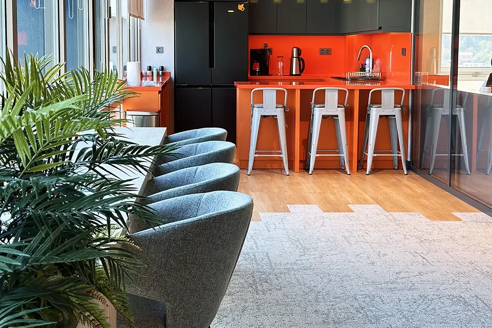 Loop Games Ofis mutfak ve bar alanı, turuncu quartz tezgah, Tolix metal bar tabureleri, koyu gri dolap ve cam bölme