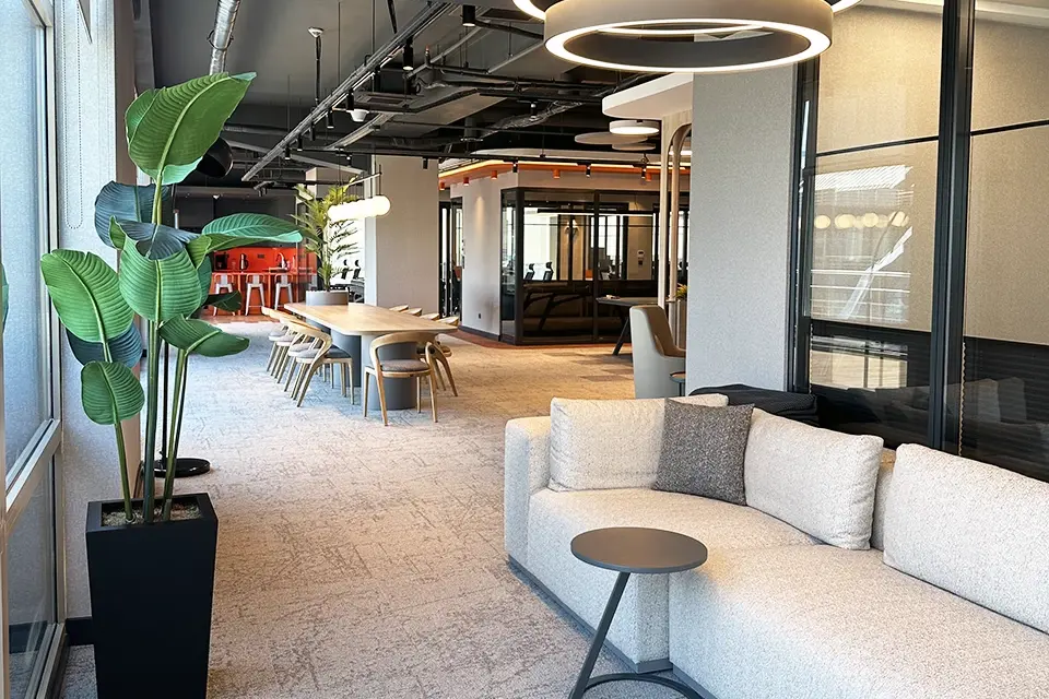 Loop Games Ofis sosyal alan, bej koltuk, bitki saksısı, çift halka LED avize ve delikli tavan paneli detayı