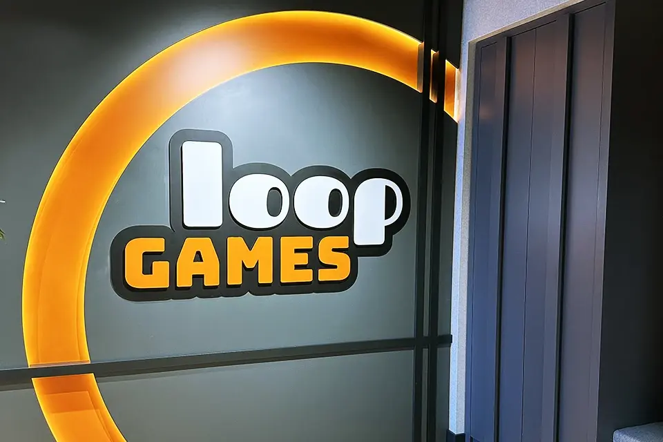 Loop Games Ofis marka duvarı, LED ışıklı turuncu halka Loop Games 3D logosu ve koyu gri duvar paneli