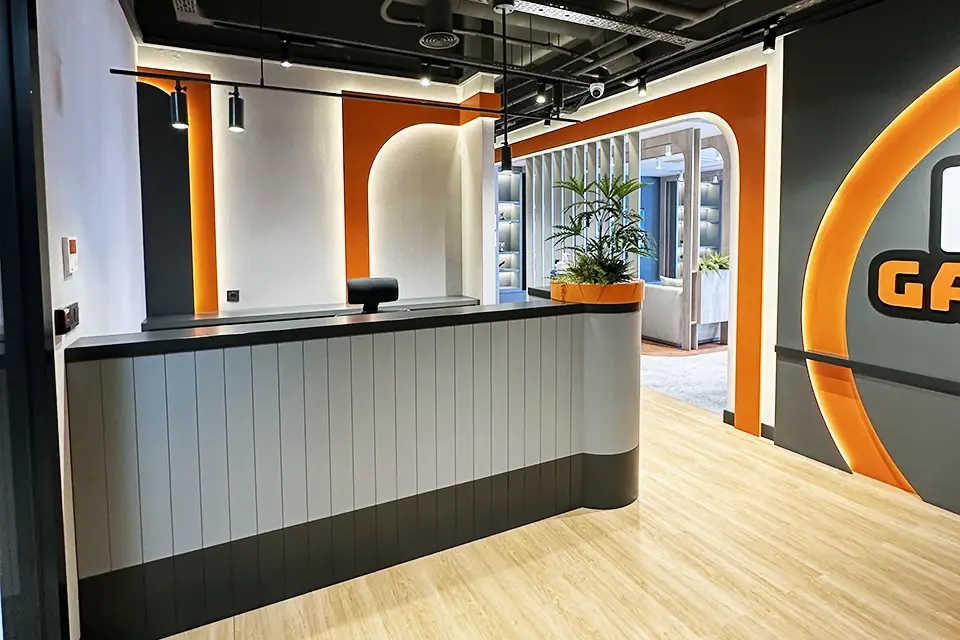 Loop Games Ofis resepsiyon alanı, dikey lamelli resepsiyon bankosu, turuncu kemerli geçişler ve bitki detayı