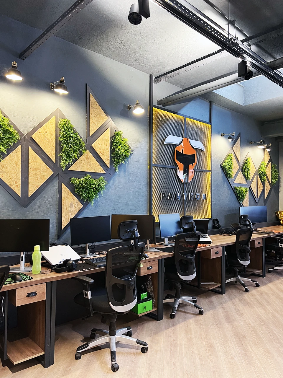Panteon Ofis duvar konsepti, OSB panel üçgen kompozisyon, yapay yeşil duvar, delikli metal Panteon logosu ve spot aydınlatma