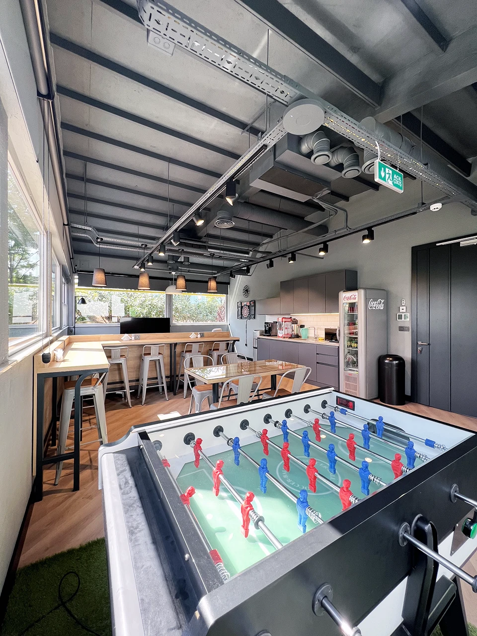 Panteon Cafe ve oyun alanı, langırt masası, ahşap bar tezgahı, Tolix tabure, endüstriyel mutfak ve suni çim zemin