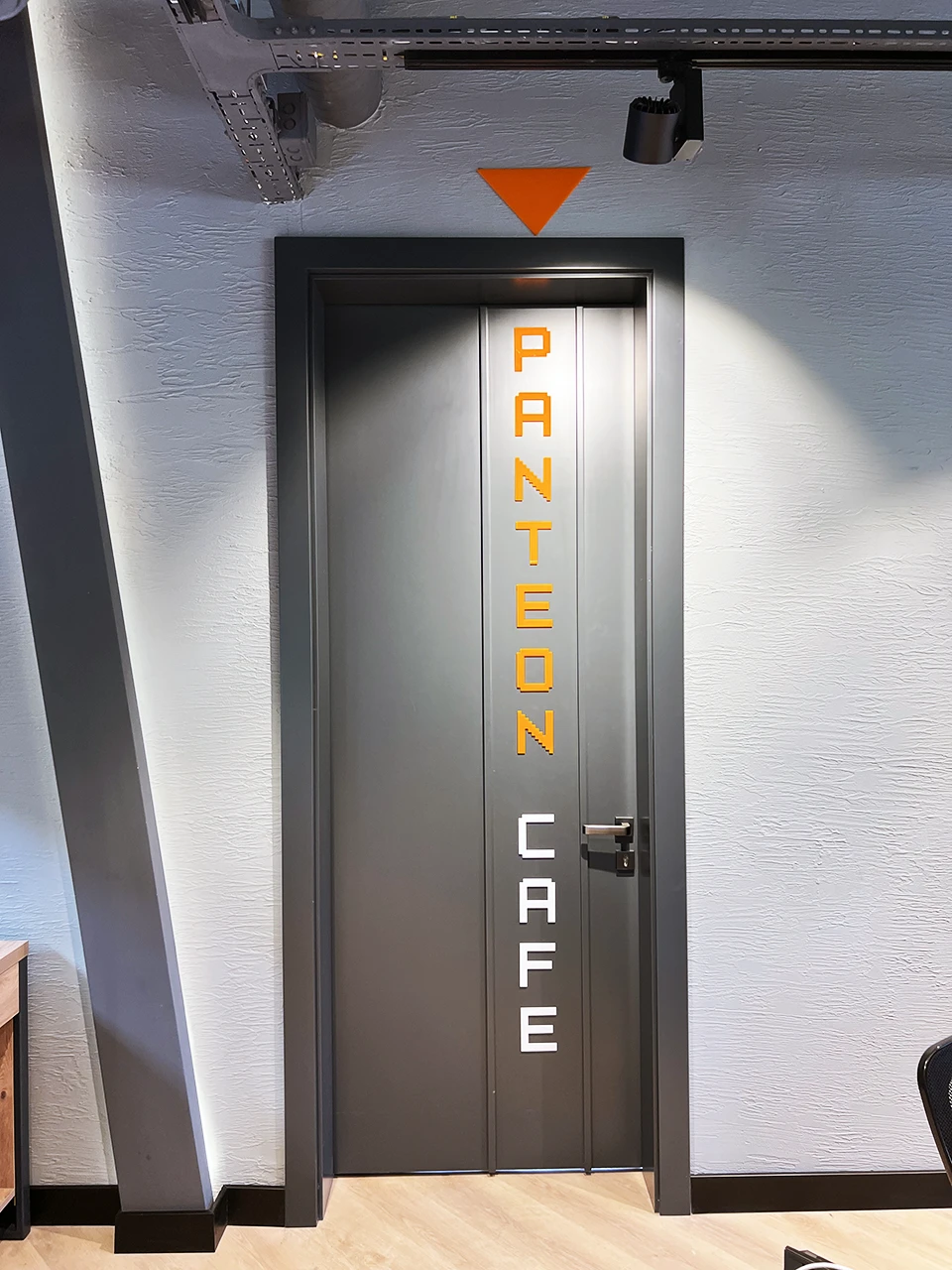 Panteon Cafe kapı detayı, piksel tipografi ile Panteon Cafe dikey yazısı, turuncu üçgen grafik ve gizli LED arkadan aydınlatma