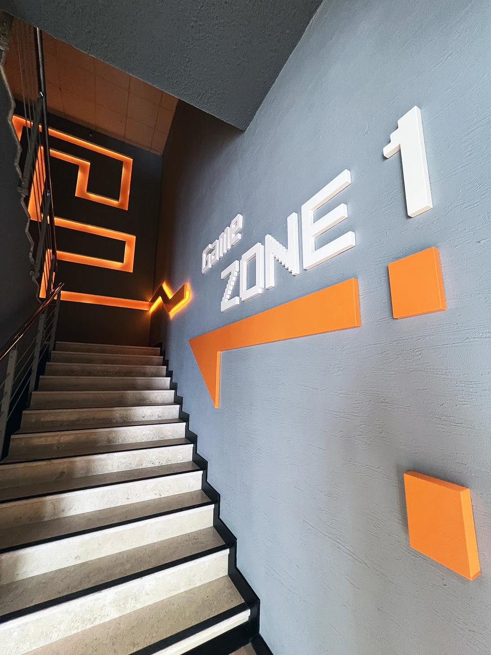 Panteon Ofis Game Zone 1 merdiven alanı, piksel tipografi duvar yazısı, turuncu ok grafik ve LED aydınlatmalı merdiven sahanlığı