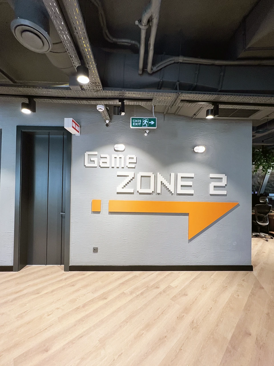 Panteon Ofis Game Zone 2 duvar tasarımı, 3D piksel tipografi, turuncu ok yön grafiği ve endüstriyel tavan detayı