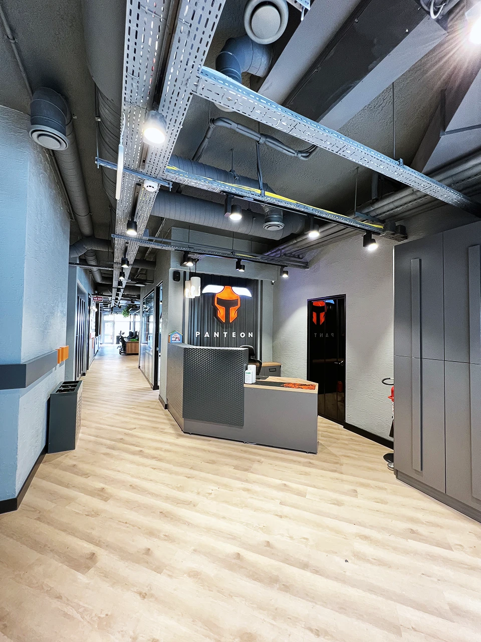 Panteon Ofis resepsiyon alanı, delikli metal resepsiyon bankosu, Panteon logosu, endüstriyel tavan tesisatı ve laminat zemin