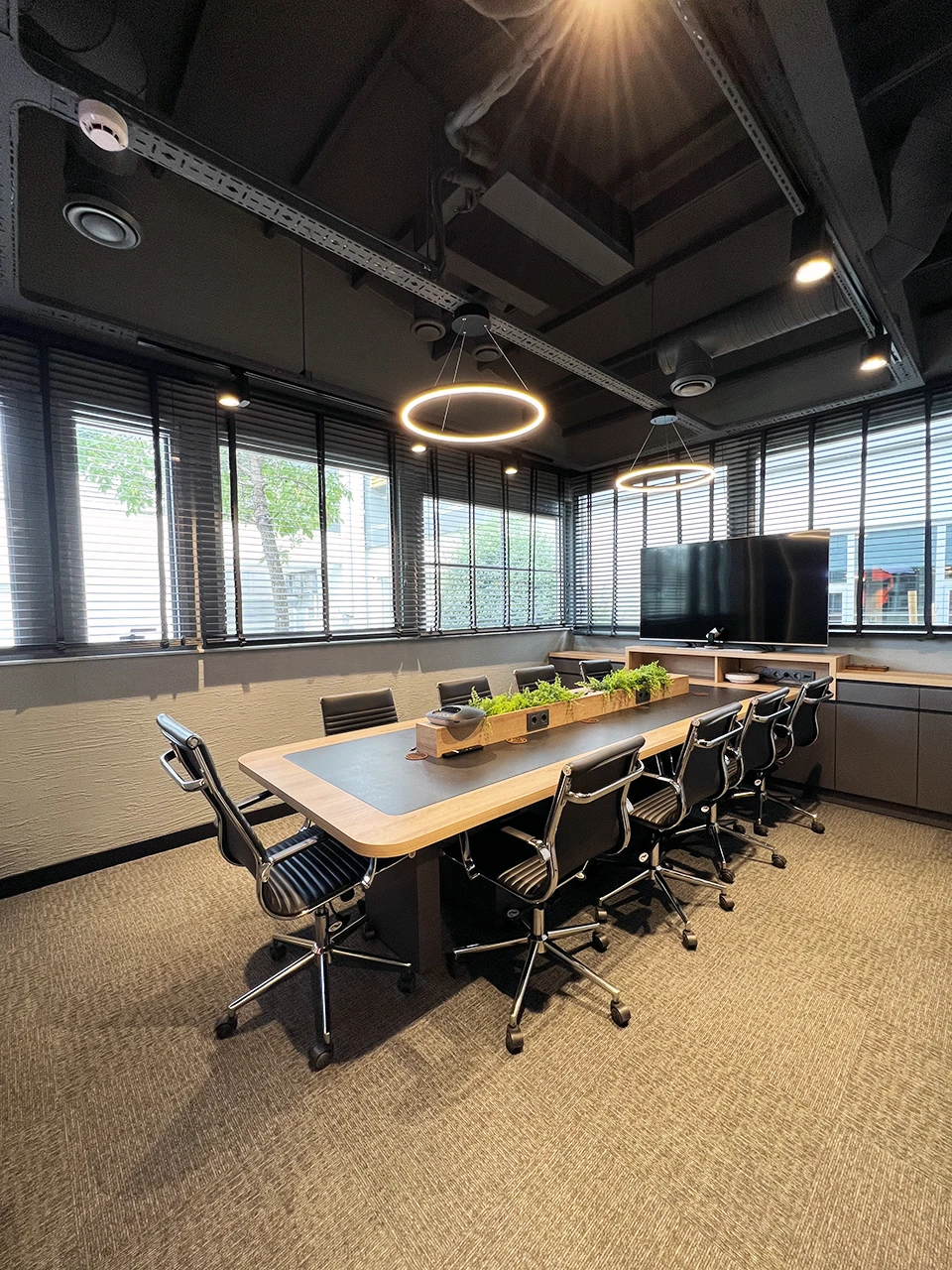 Panteon Ofis toplantı odası, ahşap toplantı masası, halka LED avize, bitki jardinyer, sunum ekranı ve halı kaplama zemin